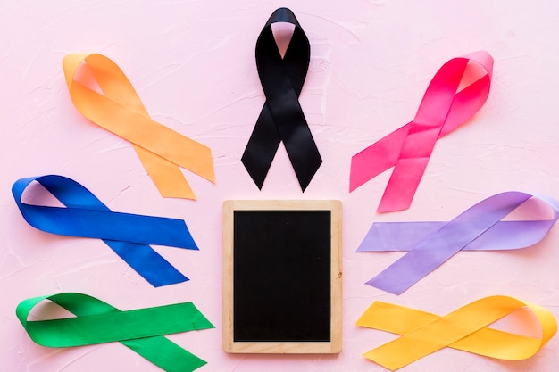 Colorful awareness ribbons around the small wooden slate on pink backdrop