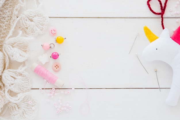 Colorful beads; spool; needle and rag unicorn on white wooden desk