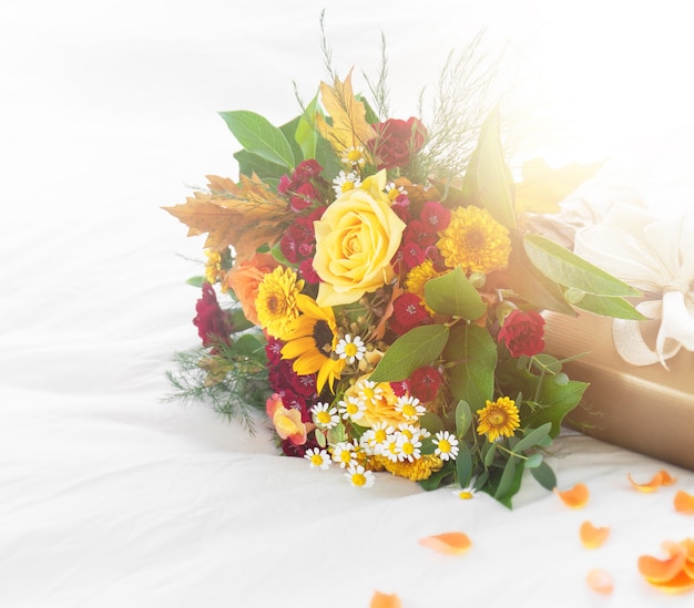 Colorful beautiful spring or summer bouquet of flowers on bed with golden gift box, holiday or surprise concept
