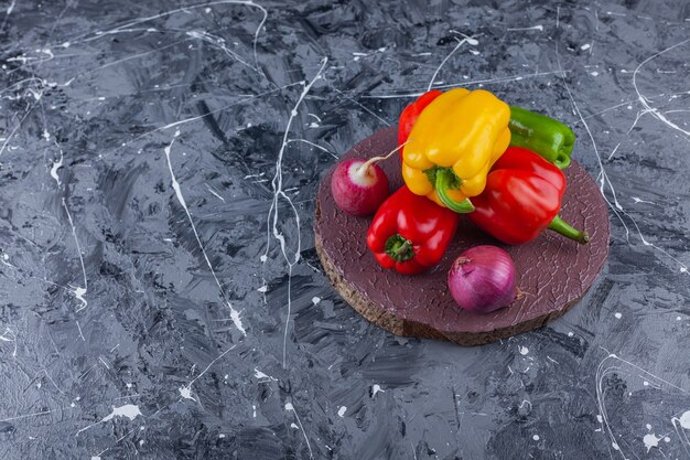 Colorful bell peppers, onionnd red radish on wood piece. 
