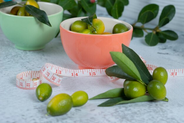 Colorful bowls of delicious juicy kumquats with measure tape on stone surface.