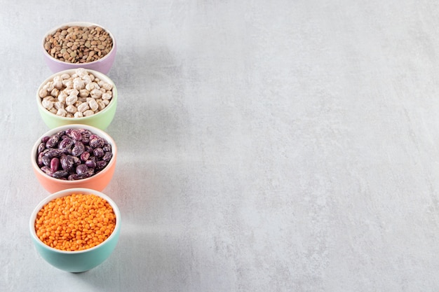 Colorful bowls full of raw lentil, peas and beans on stone surface