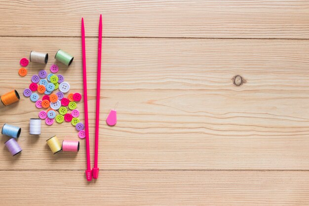 Colorful button and spool with pink knitting needles on wooden backdrop