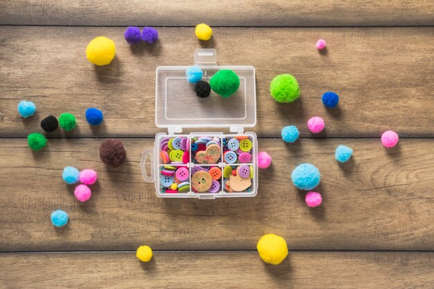 Colorful buttons in an open white box with cotton balls on wooden backdrop