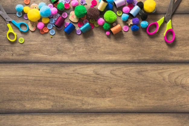 Colorful buttons; spool; scissor and cotton balls on wooden table with space for text