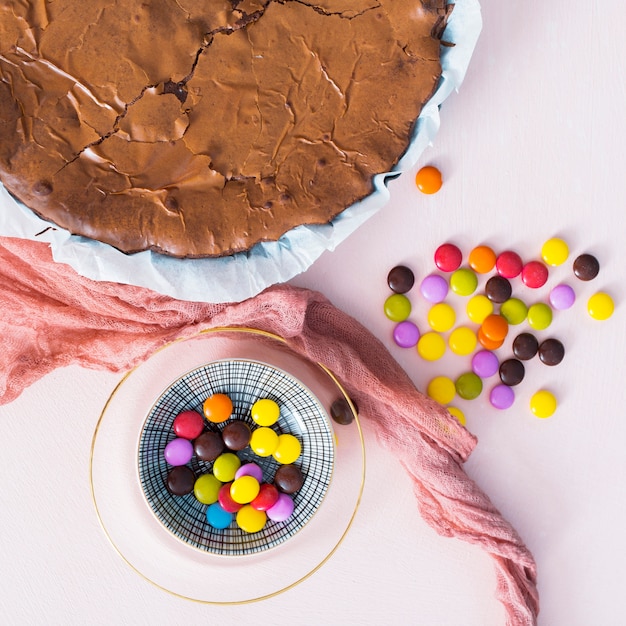 Colorful candies next to chocolate cake flat lay
