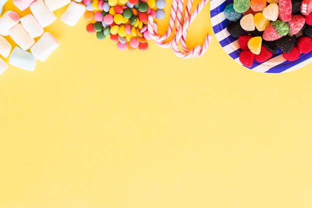 Красочные конфеты, образующие верхнюю границу на желтом фоне