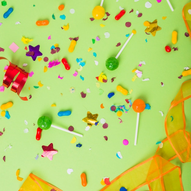 Colorful candies and lollipops with confetti and curled streamer on green background