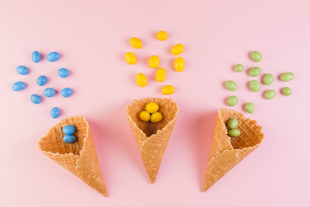 Colorful candies spilling from ice-cream waffle cone on pink background