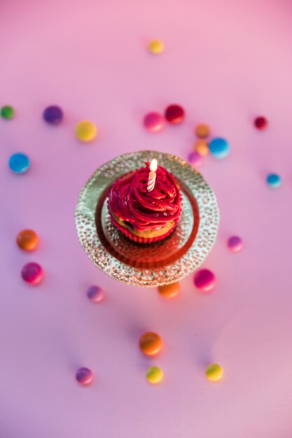 Colorful candies spread over the light cupcake on pink background