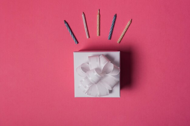 Colorful candles over the gift box with bow ribbon on pink backdrop