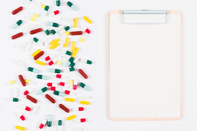 Colorful capsules and clipboard on white backdrop