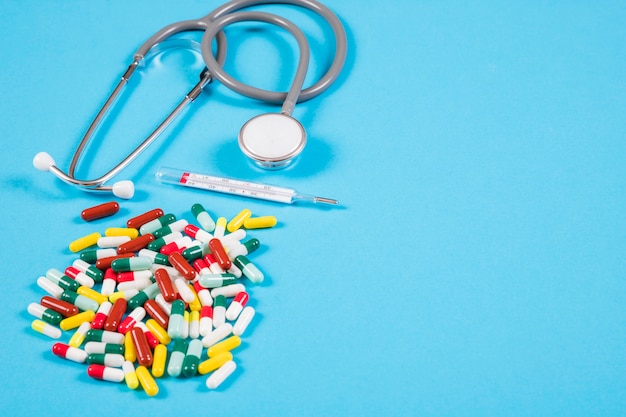 Free photo colorful capsules; pill blister; thermometer and stethoscope on blue background