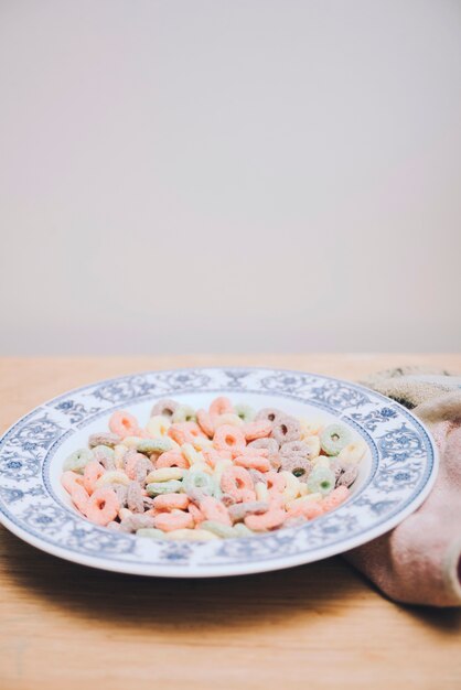 Colorful cereal in white ceramic plate on wooden desk against white backdrop