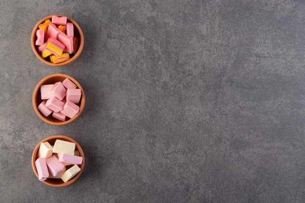 Free photo colorful chewing gums placed in clay bowls on a stone table .