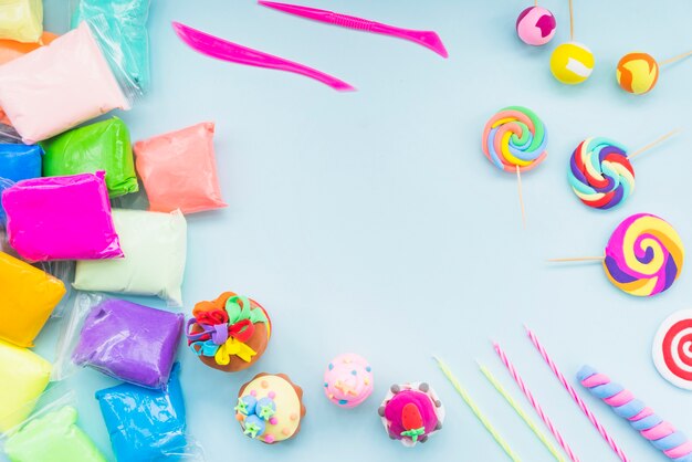 Colorful clay in plastic bag with fake cake and lollipop on blue background