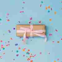 Free photo colorful confetti around the wrapped gift box tied with pink ribbon