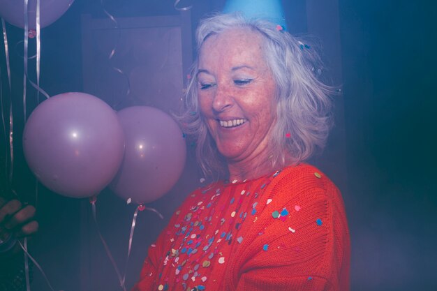 Colorful confetti over the smiling senior woman with pink balloons