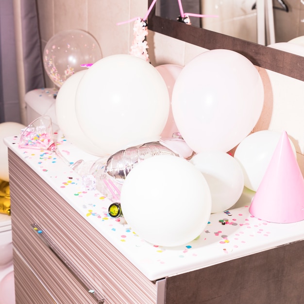 Free photo colorful confetti and white balloons on wooden desk