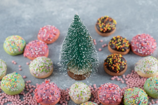 Colorful cookies decorated with sprinkles around pine tree. 