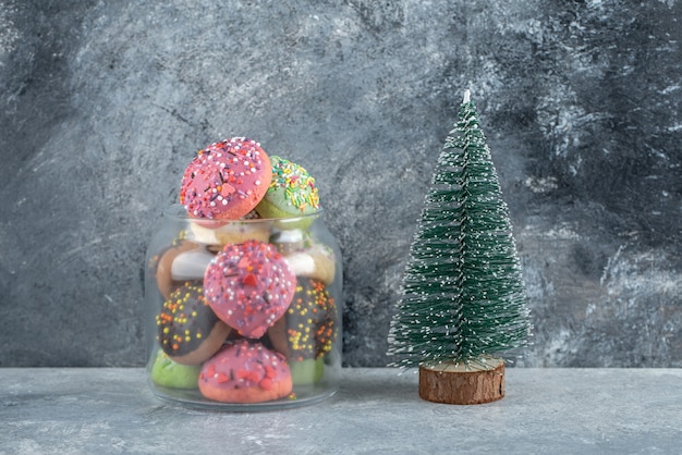 Colorful cookies with sprinkles in glass jar and pine tree. 