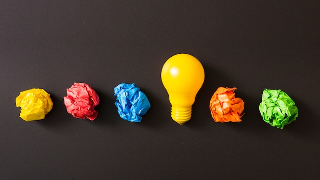 Colorful crumpled paper ball with yellow light bulb against black background