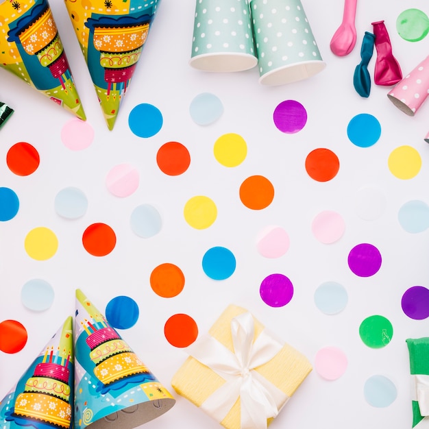 Colorful decorated confetti with party hats; gift box; balloons and wrapped gift box on white background