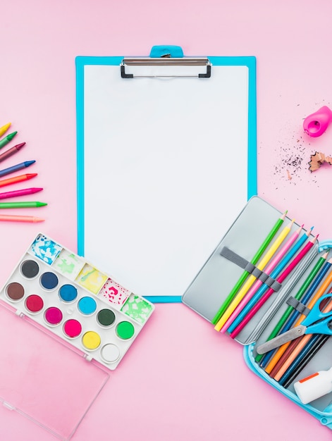 Colorful drawing accessories and clipboard over the pink background