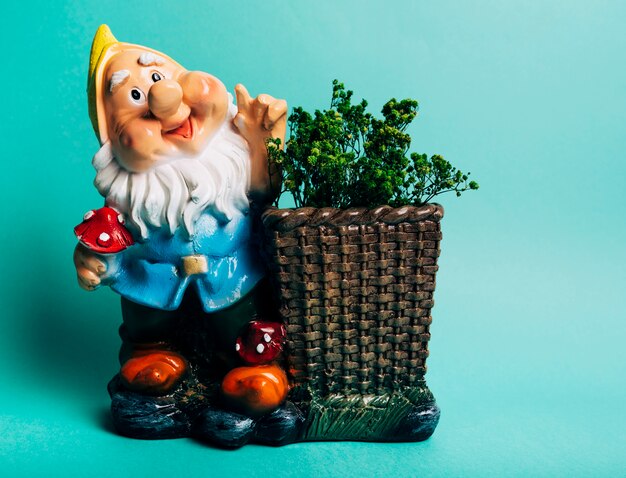 Colorful dwarf figure with plants against turquoise background