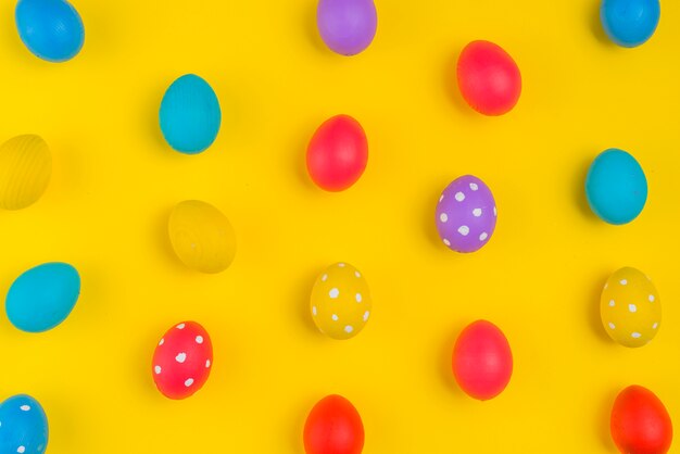 Красочные пасхальные яйца разбросаны на желтом столе
