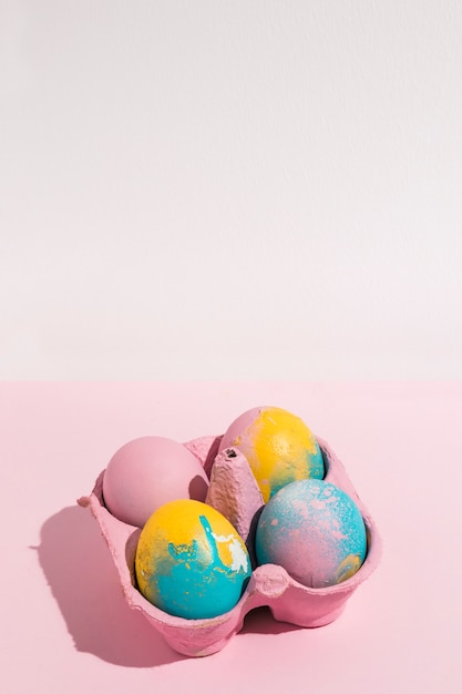 Разноцветные пасхальные яйца в небольшой подставке на розовом состоянии