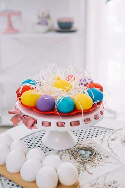 Colorful easter eggs with shredded paper on cakestand over white table