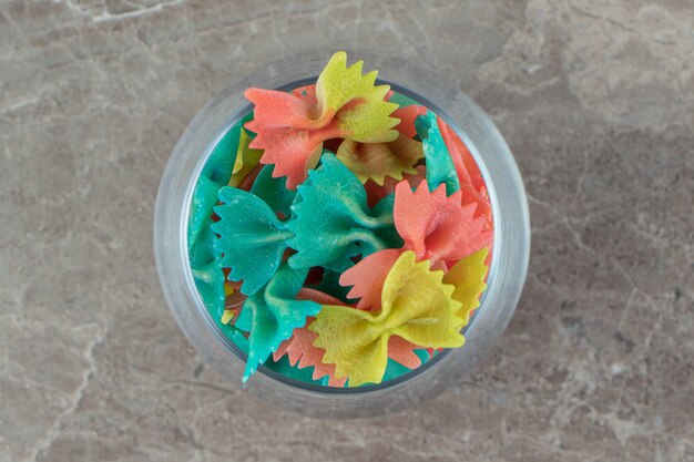 Colorful farfalle pasta in glass on marble surface.