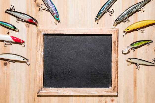 Free photo colorful fishing lures over the wooden blank slate on wooden surface