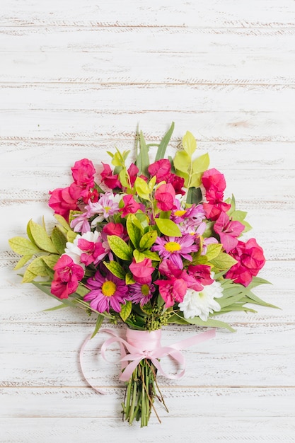 カラフルな花の花束は木製の机の上のピンクのリボンと結ばれる
