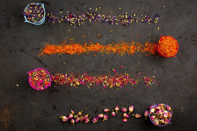 Colorful flower pieces multicolored inside pots and spread a top view on the dark desk