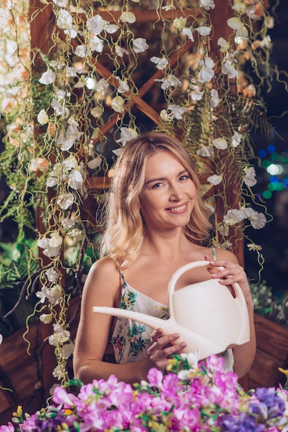 Free photo colorful flowers in front of smiling young woman holding white watering can