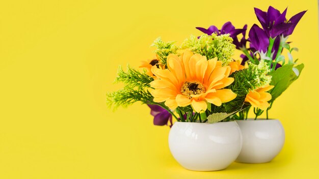 Colorful flowers in the white small vase against yellow background