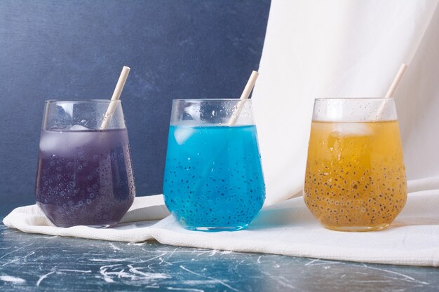 Colorful fruits in cups of drink on blue.