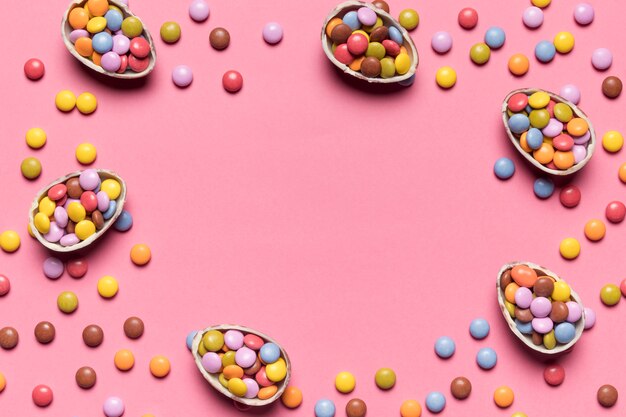 カラフルな宝石のキャンディーは中央にテキストを書くためのスペースとピンクの背景に壊れたイースターエッグでいっぱい