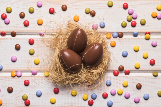 Colorful gem candies surrounded around the chocolate easter eggs nest on wooden table