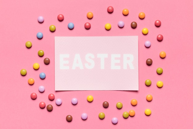 Colorful gem candies surrounded around the paper with easter word on pink backdrop