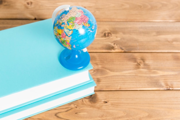 Free photo colorful globe on blue books on wooden table