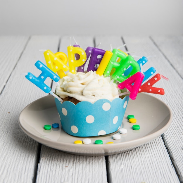 나무 테이블 위에 접시에 하나의 컵 케이크에 삽입 된 다채로운 생일 촛불