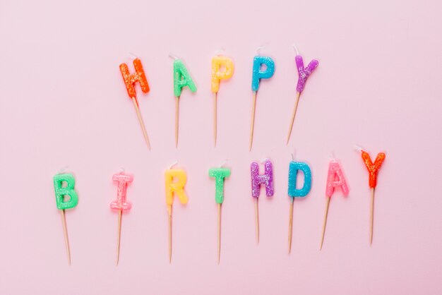 Colorful happy birthday candles with stick on pink background