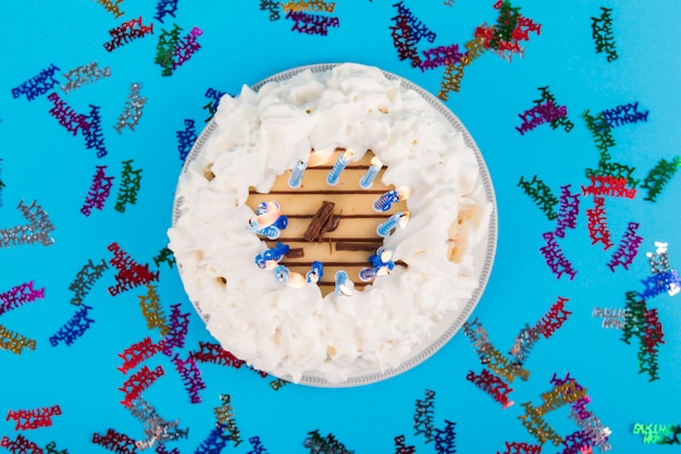 Colorful happy birthday text around the cake with lighted candles on blue backdrop