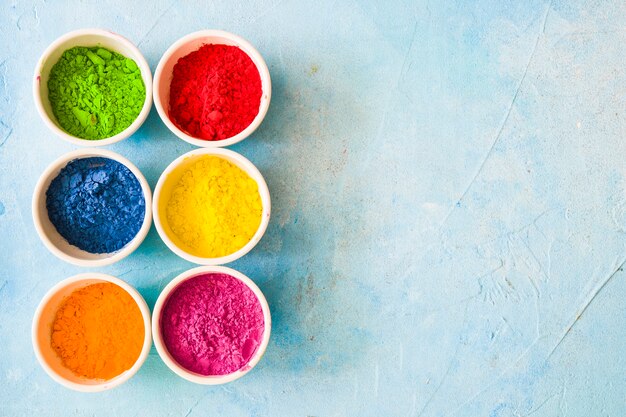 Colorful holi color powder inside the white bowls on painted blue backdrop