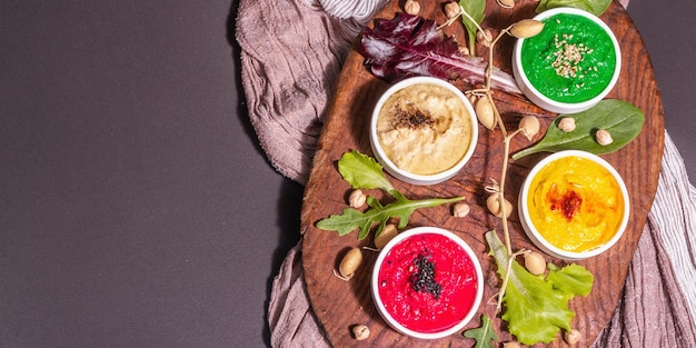 Colorful hummus bowls, healthy vegan dips. traditional middle eastern food. beets, spinach, aromatic spices. black stone concrete background, top view, banner