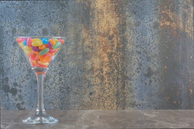 Colorful jellybean candies in glass over grey background. 