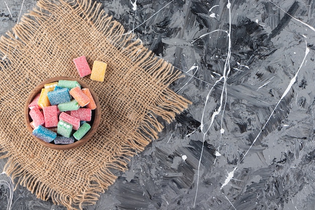 Colorful licorice in wooden bowl placed on sackcloth surface.